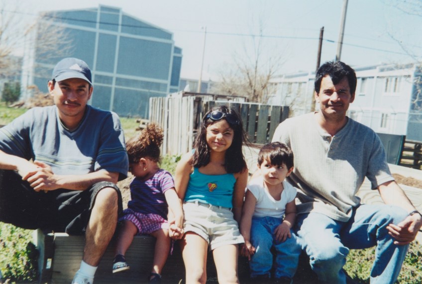 2 men and three children sit in front of a raised bed garden plot