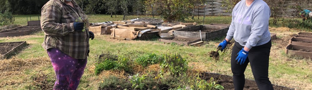 two gardeners wearing masks pose while tending to their plot in late fall 2020 at the Unite4Health garden