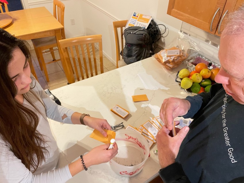 Mila and Joe horner in a kitchen measuring small seeds into paper envelopes