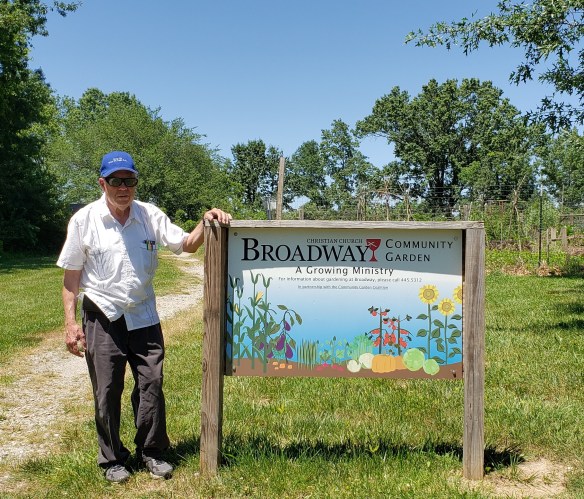 garden leader Don Day stands next to the Broadway Christian garden sign