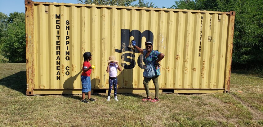Dee Campbell Carter and grandkids in front of a shipping container/storage shed at Friendship Garden