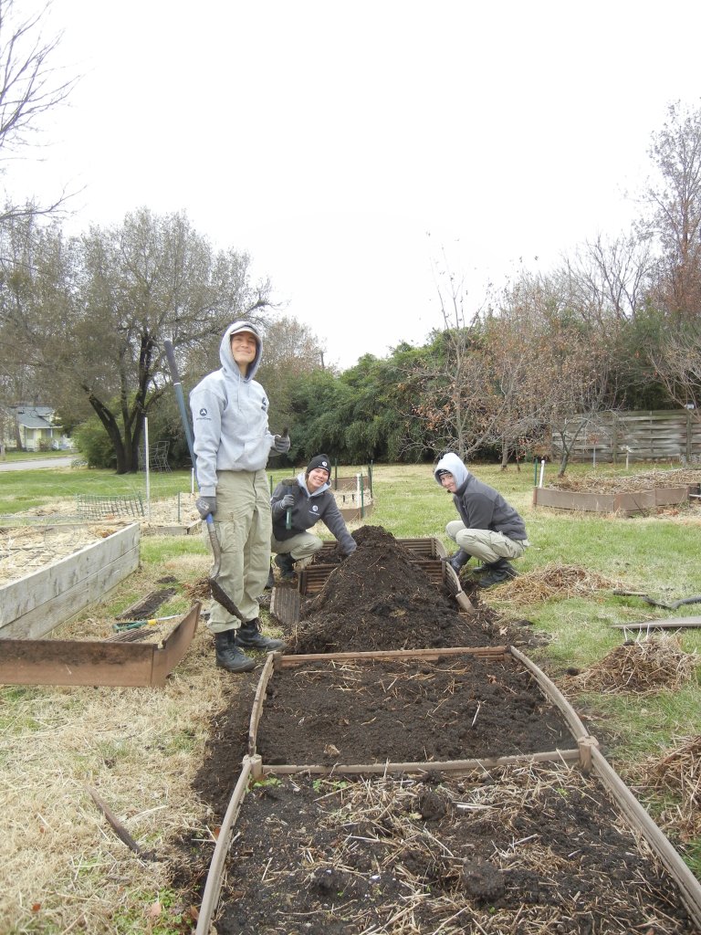 Three volunteers pause while working to spread compost in several low raised beds on an early winter day at the Unite4Health community garden.