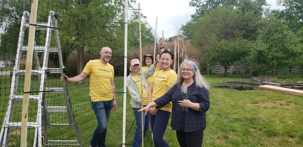 Several volunteers from ForColumbia are helping put up a tall fence of plastic netting to prevent deer from getting into Unite4Health garden.