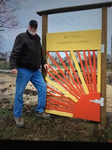 Eric Lorenz stands next to a garden gate saying Britt-Hall Community Garden
