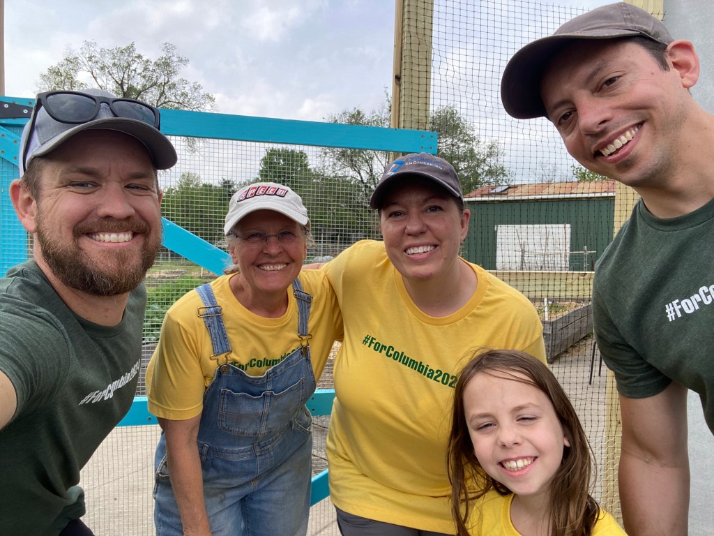 volunteers from ForColumbia 2024 pose with garden leader Cheryl next to some of the tall netted fencing meant to keep deer out of Unite4Health garden