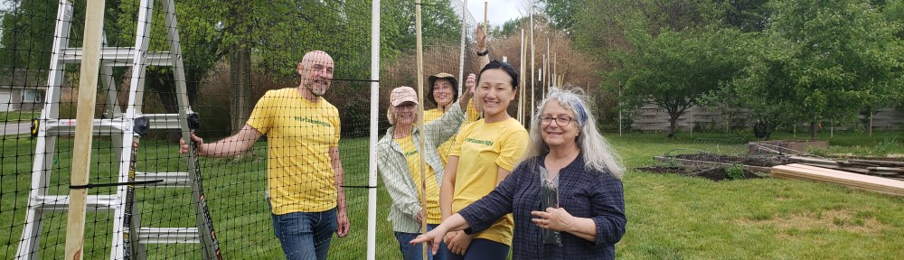 volunteers work on installing a tall netted fence to prevent deer from entering the Unite4Health garden