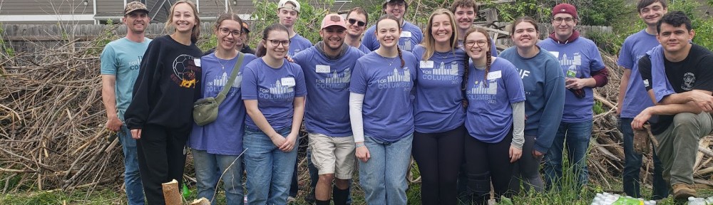 A team of For Columbia volunteers poses at Ash St. Garden in front of a mountain of cleared brush