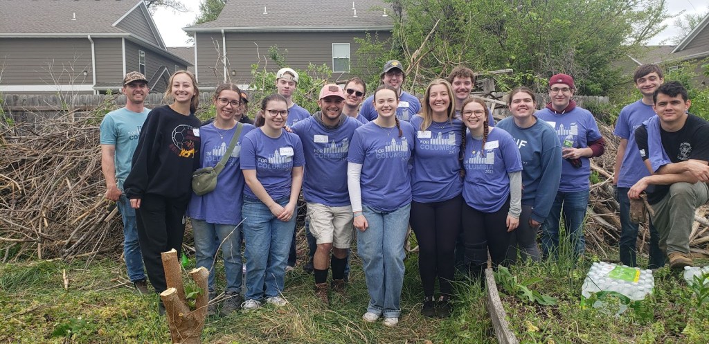 A team of For Columbia volunteers poses at Ash St. Garden in front of a mountain of cleared brush