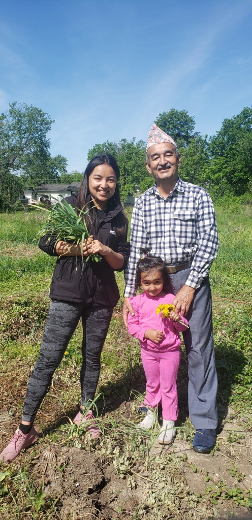 Three members of a gardening family, including a young child, pose after pulling out their fall-planted garlic from the mostly-cleared Ash St. Garden in spring