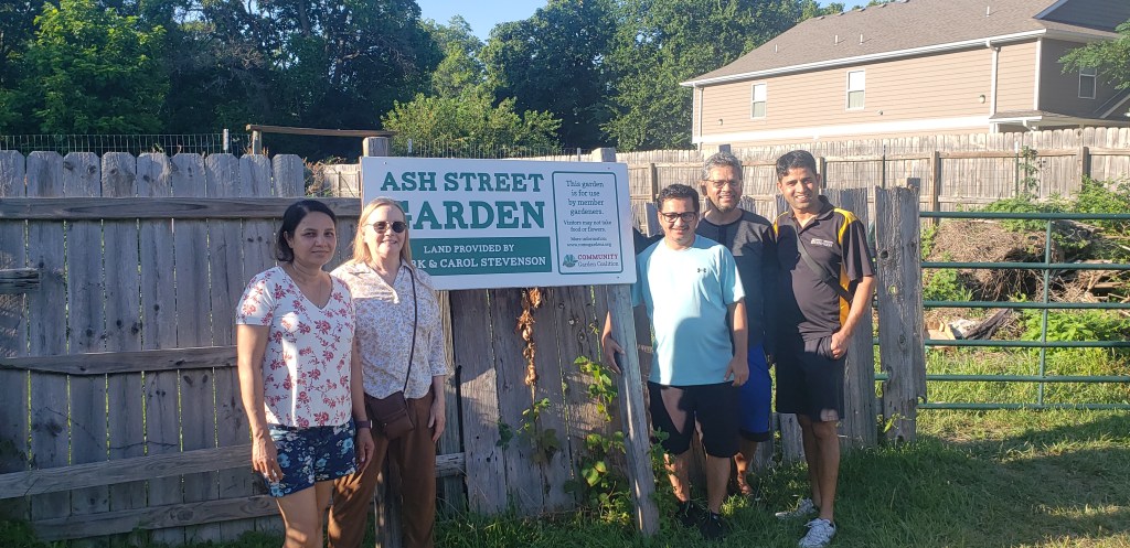 A group of people stand next to a large sign at the front of the Ash Street community garden.