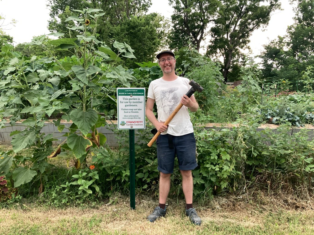 A man stands in front of a flourishing garden, next to a sign describing the garden.