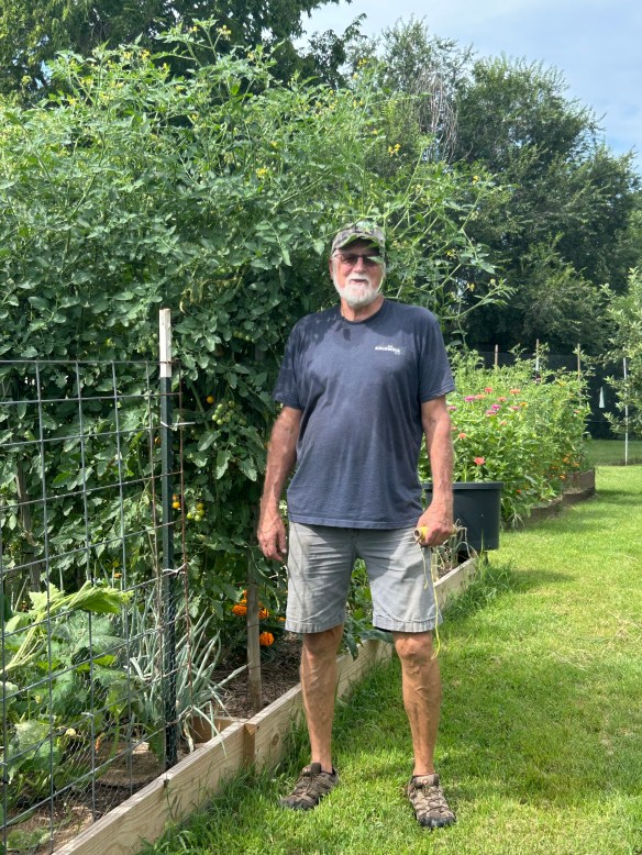 Eric Lorenz stands next to garden beds featuring a tall mass of cherry tomatoes taller than his him