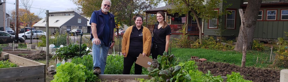 Volunteer Eric Lorenz poses behind a raised garden bed with two people in MU physical therapy scrubs