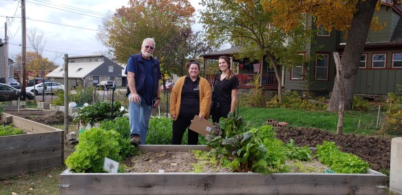 Volunteer Eric Lorenz poses behind a raised garden bed with two people in MU physical therapy scrubs